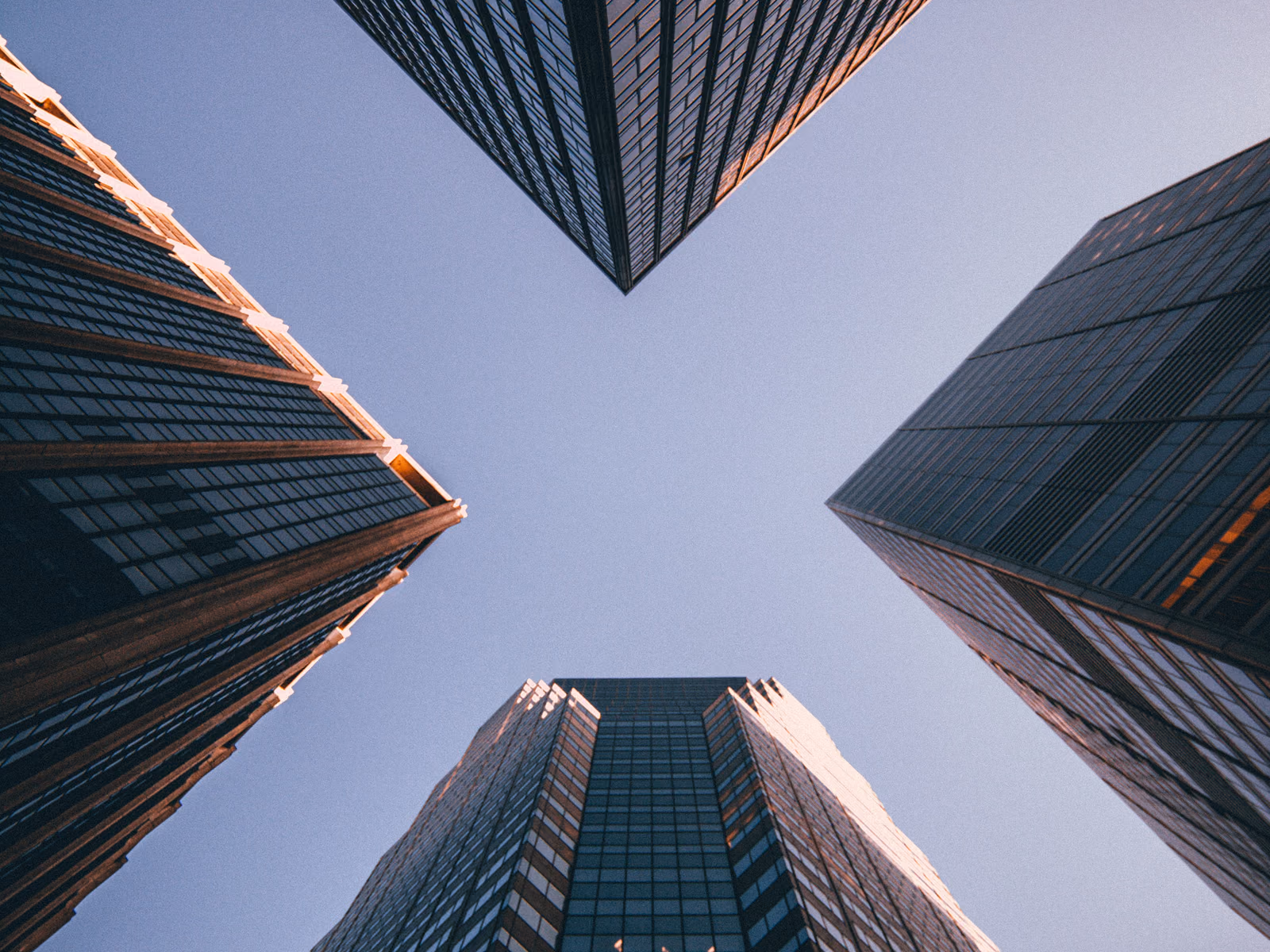 Four glass office towers seen from street level, converging on an opening of pale sky.